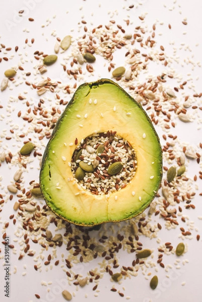 Fototapeta Close-up photo of a cut avocado on a white background sprinkled with grains.