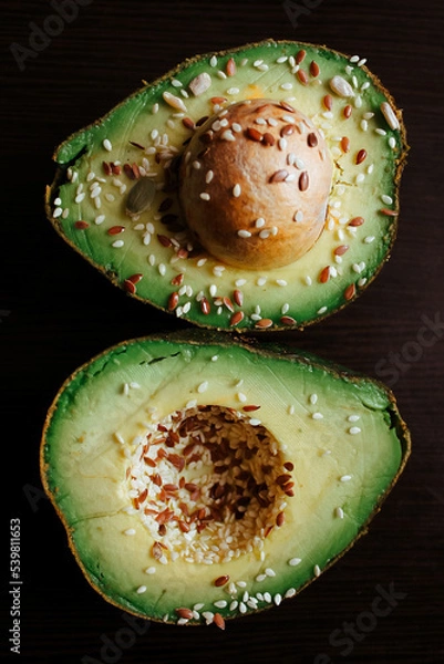 Fototapeta Close-up photo of a cut avocado on a dark background sprinkled with grains.