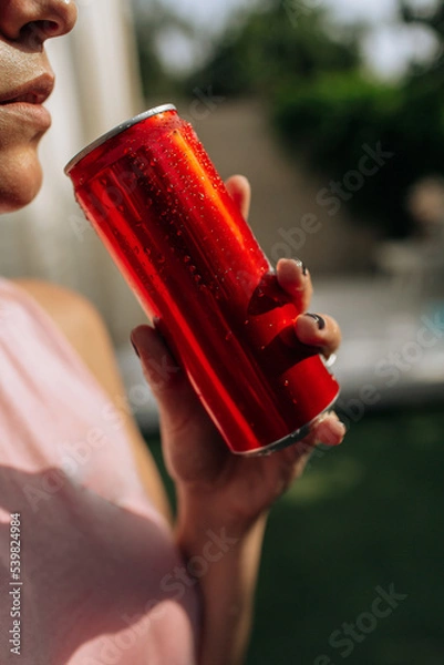 Obraz A girl on an orange background with a red tin can in her hands. Cheerful girl, advertising shooting. High quality photo