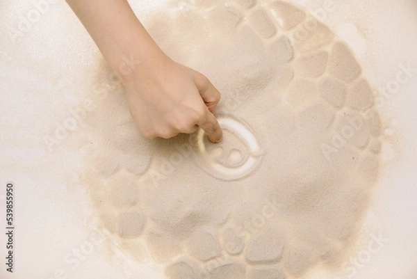 Fototapeta The child draws with fingers on the light table with quartz sand to develop motor skills
