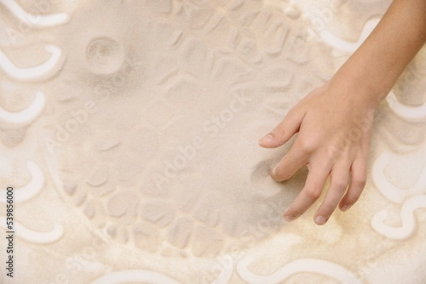 Fototapeta The child draws with fingers on the light table with quartz sand to develop motor skills