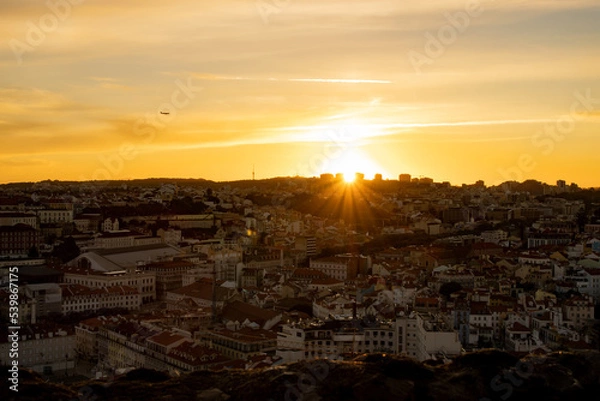 Fototapeta Lisbon city old town landscape during sunset. Golden hour in Lisbon with a view of red rooftops, blue sky and the April 25 Bridge in a distance, view of Lisbon from São Jorge Castle
