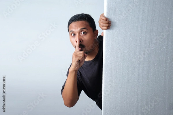 Obraz man peeking behind wall with silent gesture