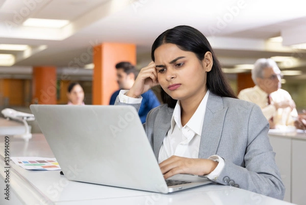 Fototapeta Thoughtful millennial professional solving problems using laptop in office.