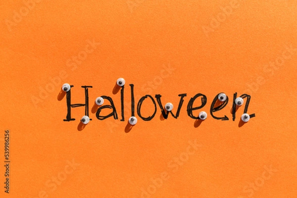 Fototapeta Halloween idea. The inscription halloween on an orange background on each letter of the eye. Festive background. Sinister background.