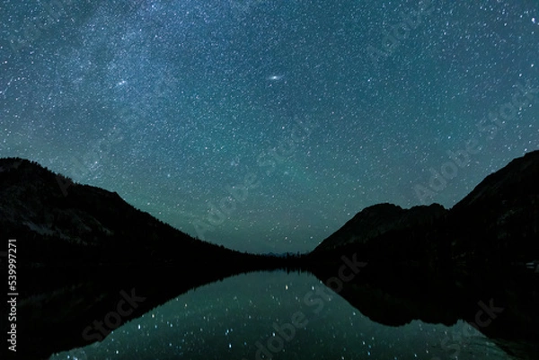 Fototapeta Toxaway Lake, located in Idaho’s Sawtooth Wilderness seen on a summer night with many stars in the sky and reflected in the water's surface.