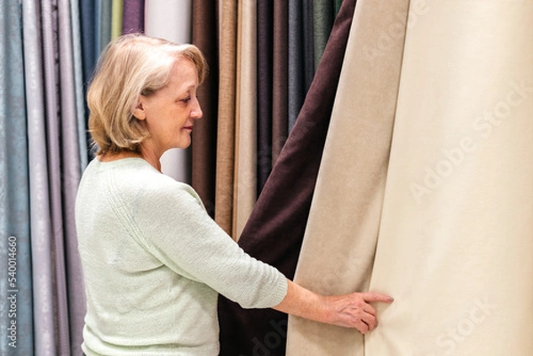 Fototapeta Woman touching fabric in store indoor. Customer choosing textures and colors of curtains in shop