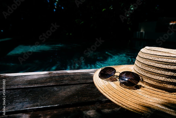 Fototapeta Straw hat and sunglasses on a wooden background, pool area. Travel and beach vacation, copy space for text.