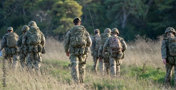 Fototapeta 8 male and female British army soldiers tabbing with 25Kg bergens across open countryside, Wiltshire UK