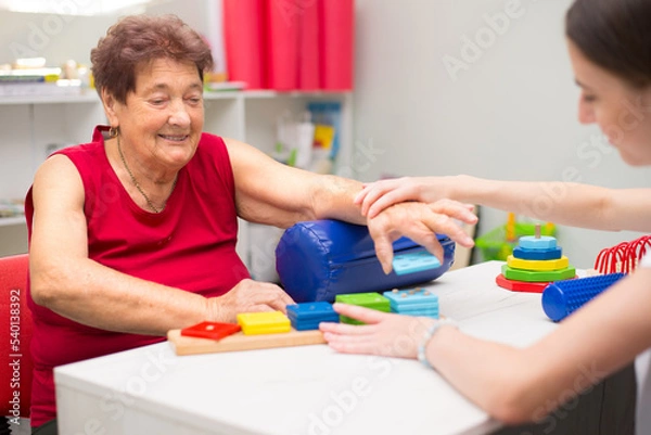 Obraz Old woman suffering from stroke exercising on physiotherapy with help of physiotherapist in the hospital