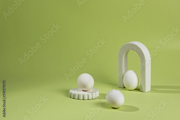 Fototapeta Composition on a green background of white podiums and arches with chicken eggs with a shadow from sunlight