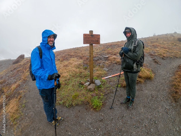 Fototapeta Adventurous athletic rain soaked male hikers standing on a trail facing the camera smiling in early spring on a cloudy day in the Pacific Northwest.