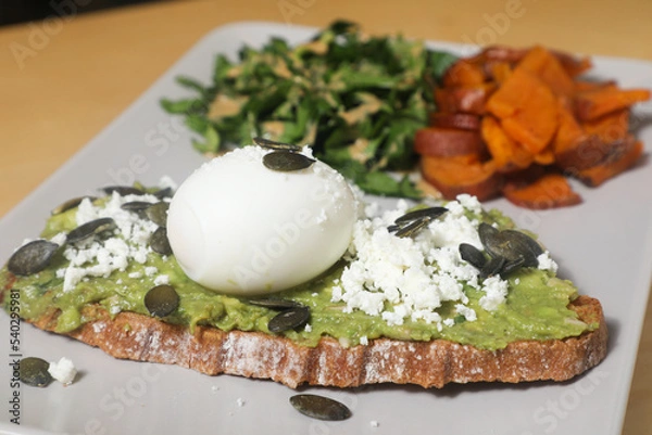 Fototapeta Tartine d'Avocat, Œuf Poché, Feta, Graines de Citrouille, accompagnée de Patates Douces et Salade