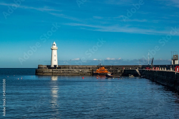 Fototapeta Donaghadee, County Down, Northern Ireland - March 09 2018. Donaghadee Harbour with its lighthouse at the mouth with a lifeboat and fishing boat moored up.