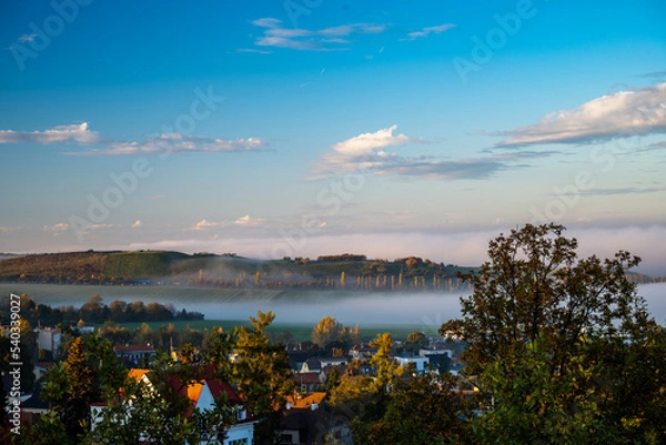 Fototapeta a large valley with a city and incoming fog