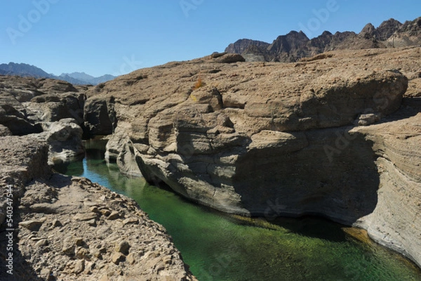 Fototapeta Fresh, clear rock pool in Hatta, an inland exclave of Dubai, United Arab Emirates. Exotic Wadi Al Qahfi on a summer day. Rugged landscape with vibrant green waters. UAE daytrip and travel destination.