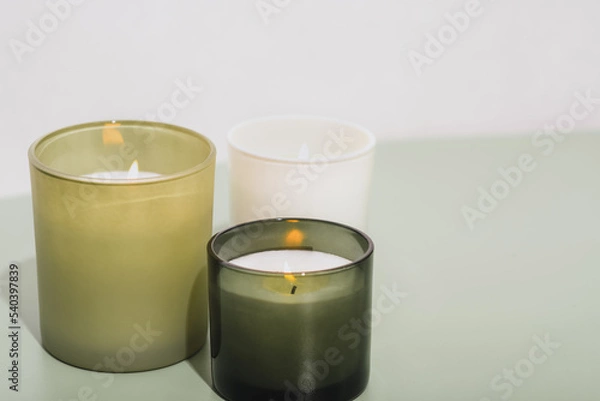 Fototapeta green scented candles burning on a table. sow wax candles with herbal aroma glowing in room. aromatherapy, cosy home, grass fragrance for house.