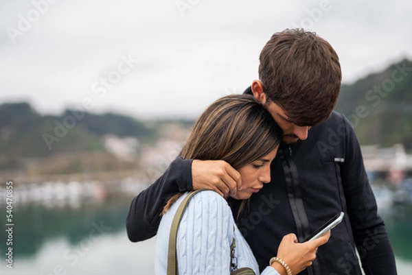 Fototapeta A young caucasian couple cuddling and checking the phone worried