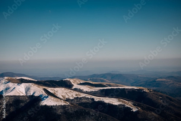 Fototapeta Panoramic view over the ski slope Poiana Brasov ski resort in Transylvania, Pine forest covered in snow on winter season,Mountain landscape in winter with the Bucegi Mountains in the background.