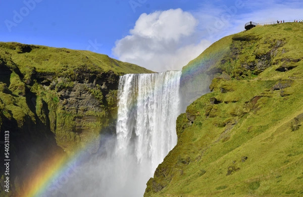Fototapeta Splashes, water and a rainbow at the Skógafoss waterfall close up in Iceland on a summer sunny day
