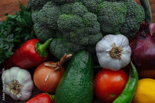 Fototapeta Raw and fresh vegetables close-up broccoli, chili pepper tomato, onion, garlic and parsley with avocado,  concept of cooking delicious and healthy food, autumn harvest agriculture food crisis