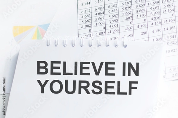 Fototapeta BELIEVE IN YOURSELF text on blue wooden background with charts