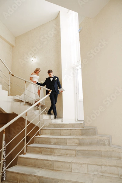Fototapeta the bride and groom go down the stairs holding hands. 