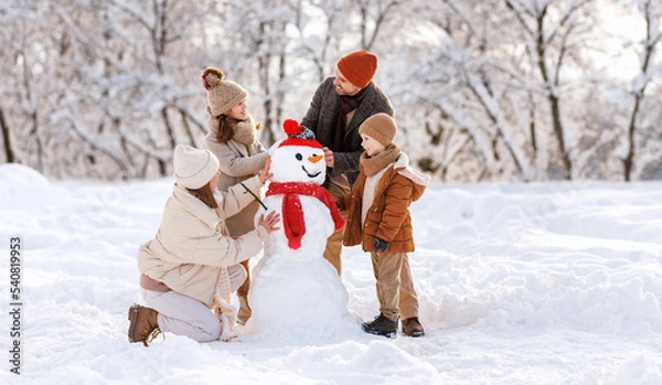 Obraz Happy children sculpting funny snowman together with parents in winter snow-covered park