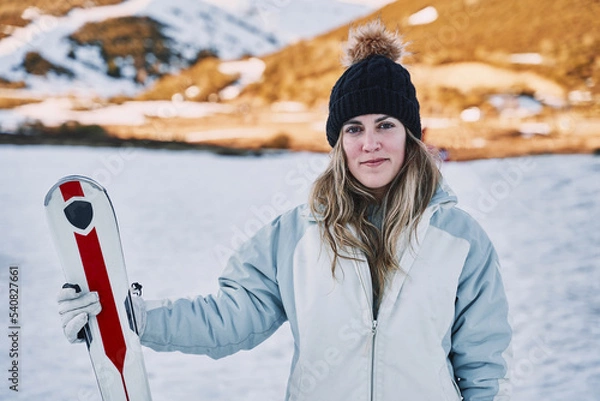 Obraz pretty girl holds some skis while looking at the camera with a slight smile.