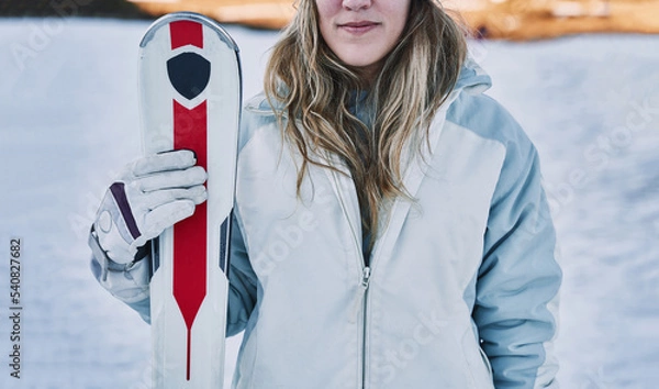 Obraz Closed shot of a pretty girl holding some skis in front of the camera.