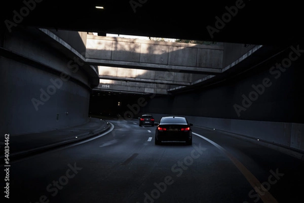 Fototapeta Black car is driving down the road in the tunnel. Traffic infrastructure, tunnel architecture, light effect.