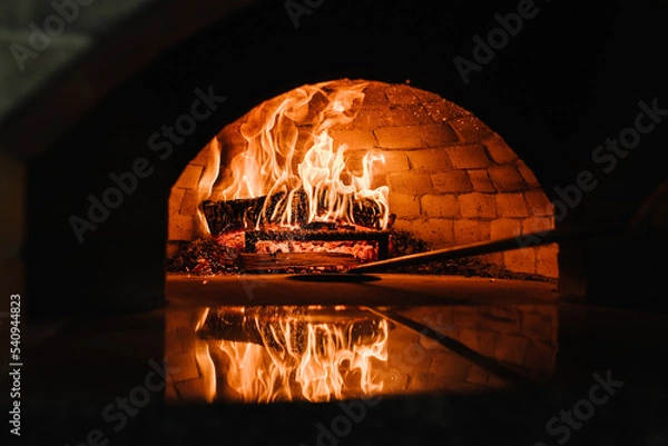 Fototapeta A traditional oven for cooking and baking pizza with a shovel. Firewood burning in the oven. Wood-fired oven. Image of a brick pizza oven with fire.