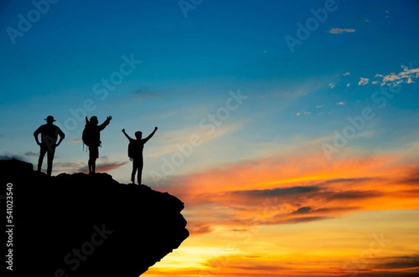 Fototapeta A silhouette of a small group of highly confident tourists standing with their arms raised under the sunrise on the top of the mountain. They were extremely happy and they showed victory.
