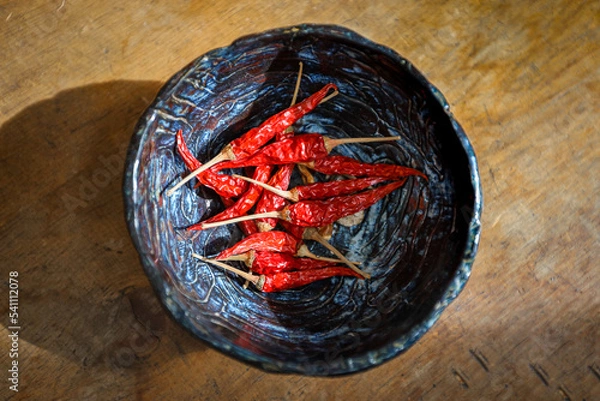 Fototapeta A bowl of red Thai Chili Peppers is seen from above on an old wooden table.
