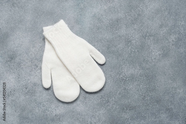 Fototapeta White knitted mittens on a gray rustic background. Down mittens. Top view, flat lay, copy space.