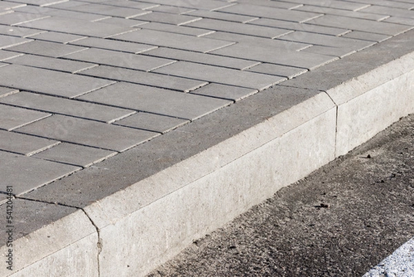 Fototapeta The sidewalk paved with concrete tiles is separated from the asphalt road by a concrete curb.