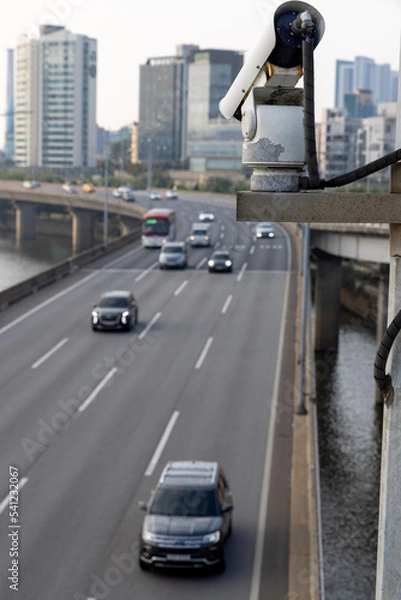 Fototapeta Security camera on the bridge watching after the car traffic, and speed control. Closeup of traffic security camera surveillance (CCTV) on the road in the big city.