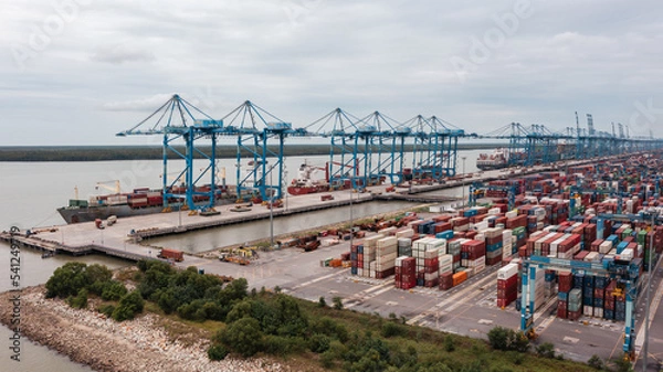 Obraz Klang, Malaysia - October 09, 2022: Cranes at the port Klang near Kuala Lumpur. Container crane at Klang Harbor. Aerial view on a container ship which is being loaded. Heavy Trucks at the Cargo bay