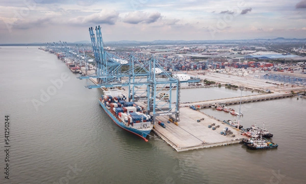 Obraz Klang, Malaysia - September 25, 2022: Cranes at the port Klang near Kuala Lumpur. Container crane at Klang Harbor. Aerial view on a container ship which is being loaded. Heavy Trucks at the Cargo bay
