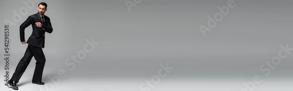 Fototapeta Professional ballroom dancer in suit dancing on grey background, banner