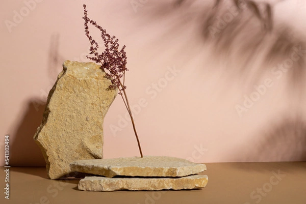 Fototapeta Background with an empty stack of stones and a dry flower on a beige background. Stone podium for cosmetic products. Pedestal for product presentation.