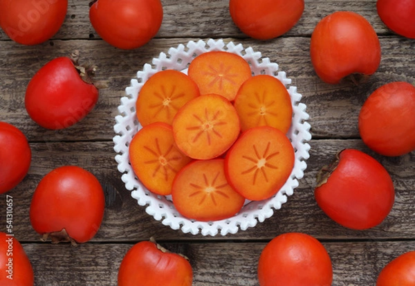 Obraz Slices of persimmon fruit in a bowl on a wooden background. Top view. Directly above photo.