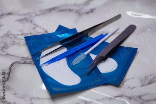 Fototapeta Set of eyelash extension tools with patches on a light marble background