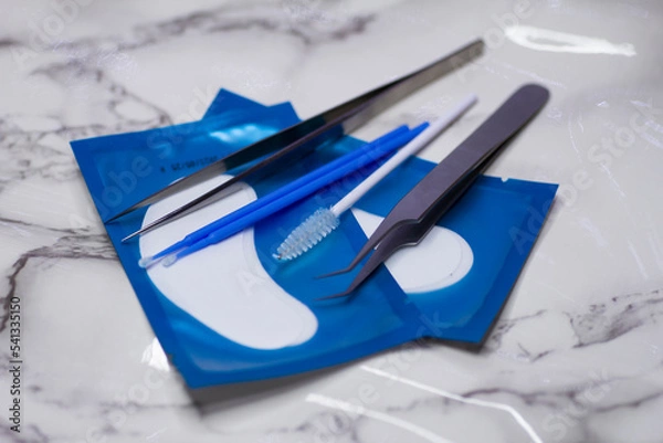 Fototapeta Set of eyelash extension tools with patches on a light marble background
