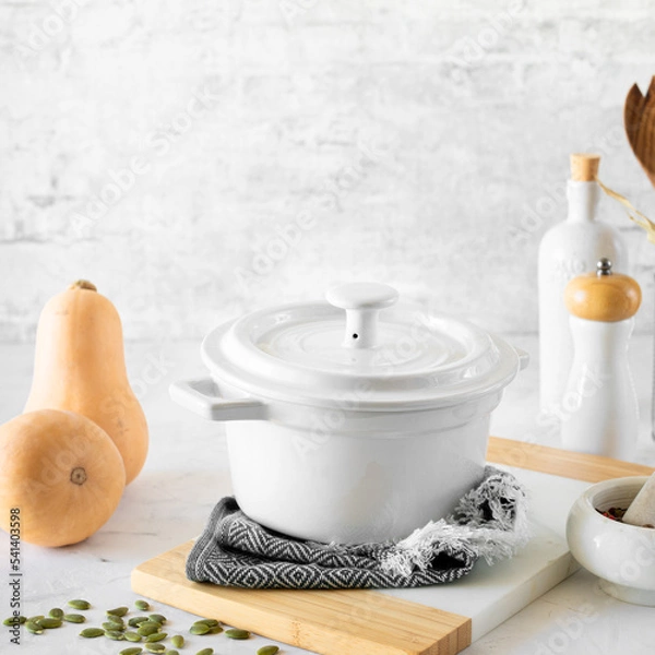 Fototapeta White saucepan, kitchen utensils, ingredients for making fresh pumpkin soup on a white background. copy space
