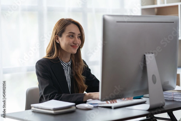 Fototapeta Asian businesswoman sitting in front of a computer screen analyzing and calculating the earnings of marketing partners in the company's office.