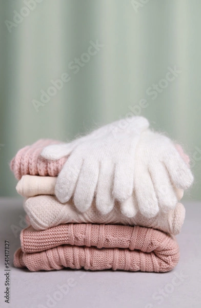Fototapeta Warm woolen gloves of white color are lying on a stack of knitted things. Vertical photo.