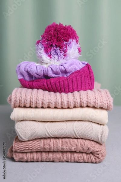 Fototapeta A bright knitted hat is lying on a stack of sweaters. Vertical photo. Warming clothes.