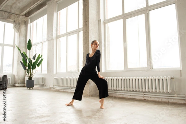 Fototapeta Modern female dancer in black outfit practices in a dance studio