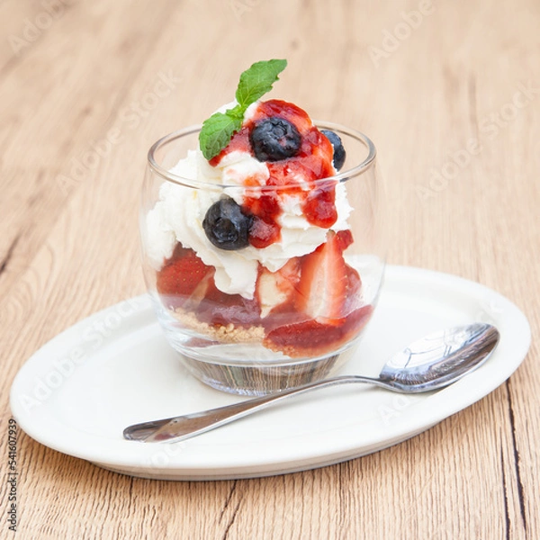 Fototapeta Homemade vanilla ice cream parfait with strawberry, blueberry, whipped cream, cookie crumble and sauce